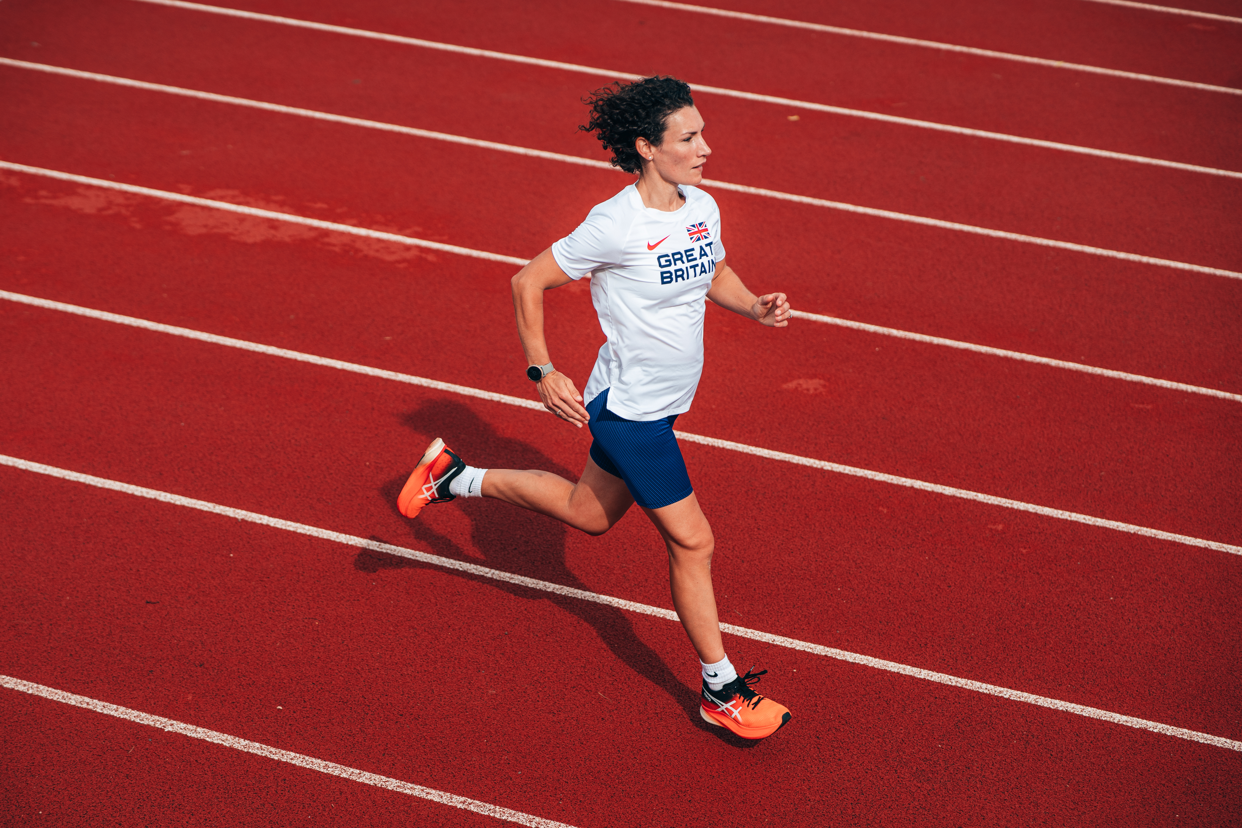 Sophie is running in profile on a red race track, wearing a Team GB top and blue shorts.