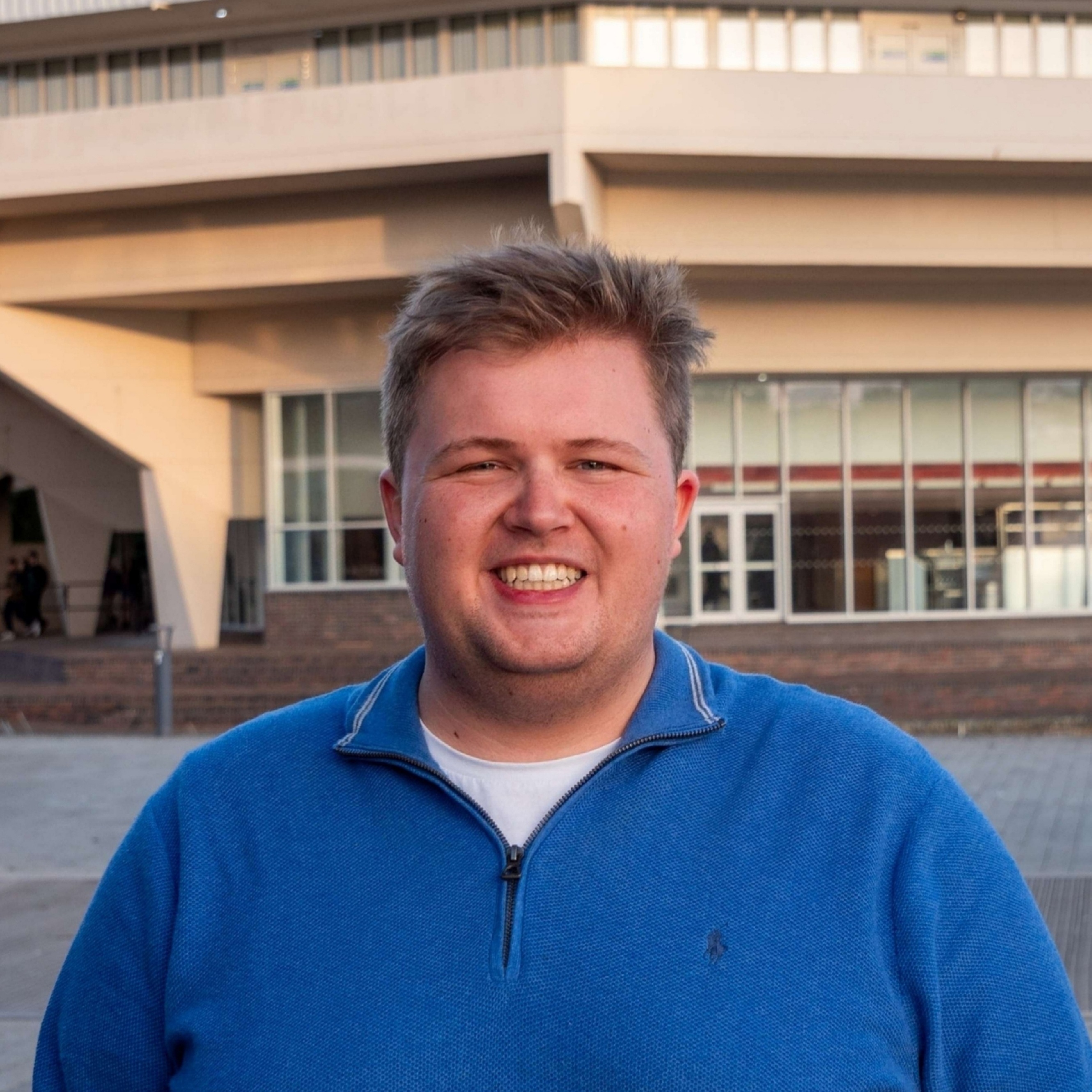 Thomas is outside, in a blue top smiling at the camera