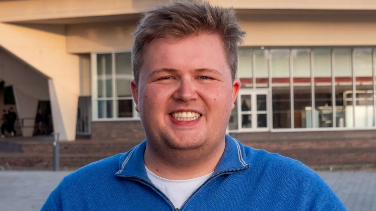 Thomas is outside, in a blue top smiling at the camera