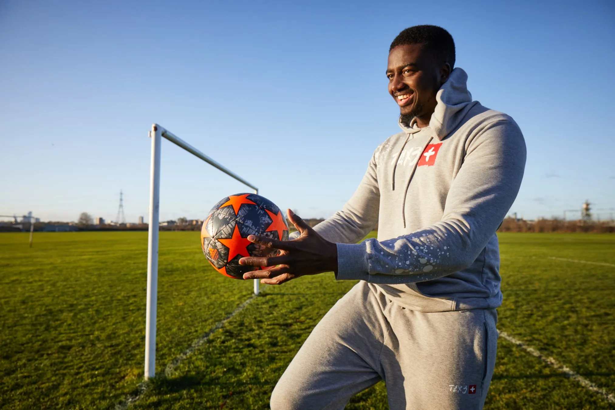 Image for the Movement for Change programme, showing a happy, hopeful-looking young man with a ball, standing in a sports pitch.